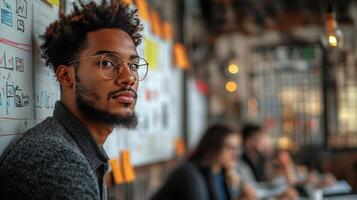 Young man with glasses sitting in creative workspace during brainstorming session with colleagues photo