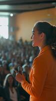 A woman in an orange suit is giving a speech to an audience photo