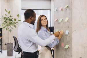Diverse team collaborating, sharing ideas through colorful sticky notes on glass wall, representing innovative workplace communication photo
