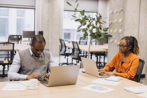 Diverse business team collaborating, using laptops and brainstorming strategic plans in modern, vibrant office environment photo