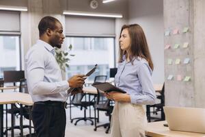 Businessman and businesswoman engaging in a work discussion in a modern office, utilizing a tablet and clipboard for effective collaboration photo