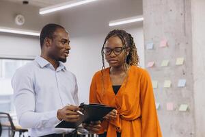 Two young african american professionals reviewing notes on clipboard in bright modern office space photo
