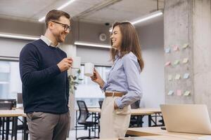 Professional team drinking coffee, conversing near glass windows during workplace break photo