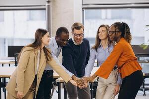 Diverse businesspeople joining hands in office, symbolizing teamwork, collaboration, and unity in achieving shared goals photo