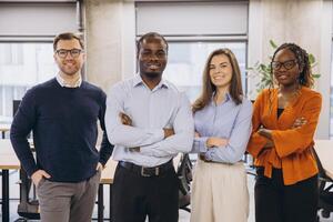 Multi ethnic businesspeople standing together with arms crossed, showing teamwork and confidence in a bright office environment photo