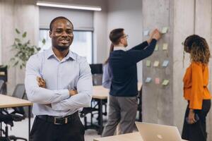 Smiling African american male, professionals working together in a contemporary office, exchanging ideas and organizing tasks with sticky notes on a concrete wall photo
