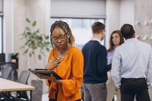 African american businesswoman holding a folder, diverse professionals collaborating during high tech meeting, discussing strategy while using digital devices in modern workplace environment photo