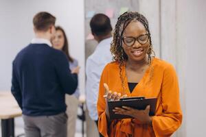 Smiling african american businesswoman holding a folder, group of diverse business professionals collaborating in a modern office environment, focusing on teamwork and effective communication photo