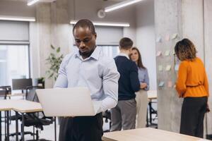 African american man using laptop, professionals collaborating in contemporary workspace, leveraging digital tools and sharing insights during team meeting photo
