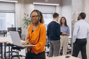 African american woman using laptop, diverse professionals collaborating with digital devices, sharing insights during strategic meeting in modern workplace environment photo