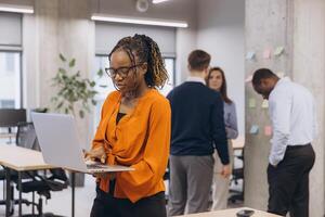 African american woman using laptop, professional team collaborating in sleek workspace, sharing ideas while utilizing digital devices for efficient workplace communication and teamwork photo