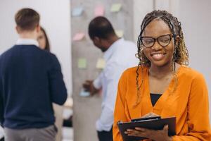 Smiling african american businesswoman holding a folder, diverse professionals collaborating in modern office, brainstorming strategies, sharing insights, driving business innovation and teamwork photo