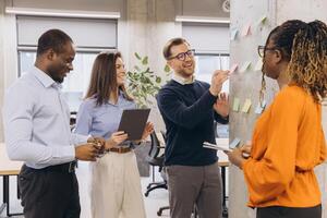 Diverse business team collaborating on a project, using sticky notes on a wall in a modern office environment photo