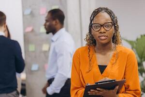 Smiling african american businesswoman holding a folder, diverse group of business professionals collaborating in a modern office setting, focusing on teamwork and innovation for successful project photo