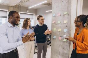 Professional team applauding female executive following compelling presentation near whiteboard wall in contemporary workspace photo