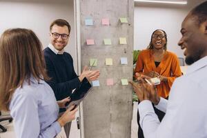 Diverse businesspeople discussing new project ideas using sticky notes on a wall in a modern office photo