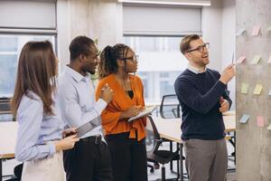 Diverse businesspeople brainstorming and discussing ideas using colorful sticky notes on a wall in modern office photo