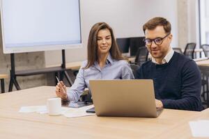 Two business professionals working together, using laptop and analyzing data in contemporary office space photo