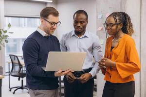 Multi ethnic businesspeople collaborating on a project, looking at a laptop and discussing ideas in a modern office environment photo