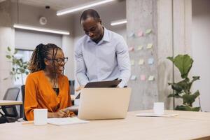 Professional african american team collaborating, using digital devices at modern workspace, exchanging innovative concepts across diverse backgrounds photo