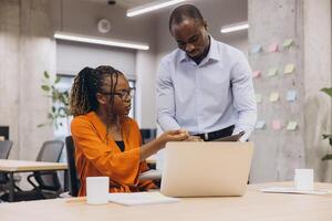 Two African american businesspeople collaborating, working on laptop near colorful sticky notes, modern workspace setting photo