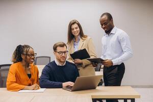 Professionals collaborating through digital devices, working together in modern, bright office space with diverse team members photo