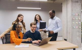 Professional team collaborating, discussing project details, working together on laptop in modern, bright office setting photo