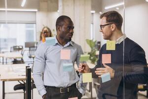 Two business professionals discussing ideas in a contemporary office environment, surrounded by colorful sticky notes on a glass wall photo