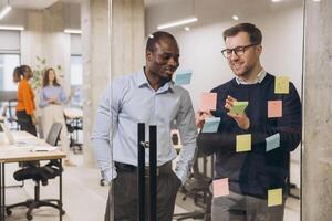 Collaborative business meeting with professionals brainstorming, using sticky notes on glass wall, modern workspace environment photo