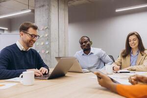 Multiethnic group of professionals working together at conference table with laptops and documents. Office workers sharing ideas during casual meeting photo