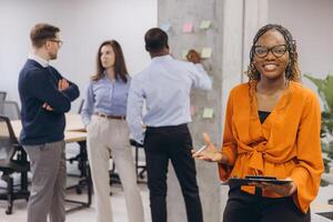 Smiling african american businesswoman holding a folder, professional team collaborating during strategy session, brainstorming with sticky notes, representing workplace diversity and innovation photo