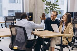 Diverse business team in a modern office environment celebrating success with a high five, showcasing teamwork and collaboration in a professional setting photo