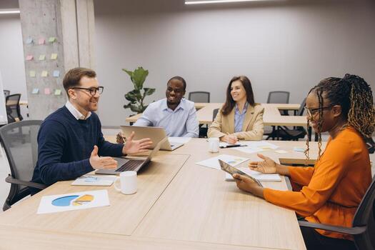 Diverse professionals collaborating, reviewing data charts and digital devices during strategic planning session in modern workplace setting photo