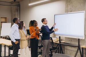 Diverse group of professionals engaging in a collaborative discussion around a large digital screen in a modern office setting photo