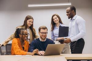 Professional team collaborating around laptop, displaying cultural diversity and teamwork in modern office environment photo
