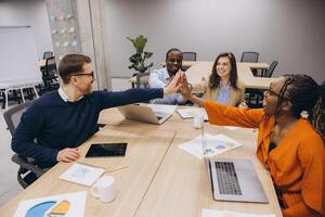 Professional team collaborating during meeting, sharing insights across conference table with laptops and strategic planning documents photo