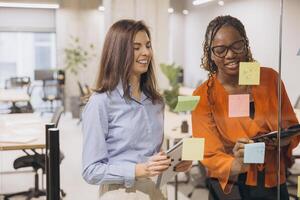 Business colleagues brainstorming, placing colorful sticky notes while planning strategy near transparent office partition photo