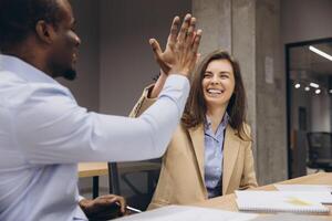 Two business professionals sharing a high five in a modern office, symbolizing teamwork, collaboration, and success in a diverse workplace photo