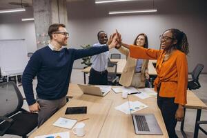 Diverse group of business professionals high fiving in a modern office setting, symbolizing teamwork, collaboration, and success in a corporate environment photo