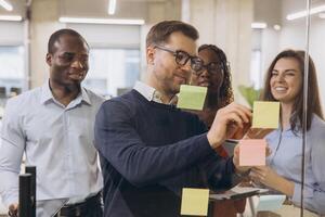 Diverse group of professionals engaging in a collaborative brainstorming session, using sticky notes on a glass wall in a modern office environment photo