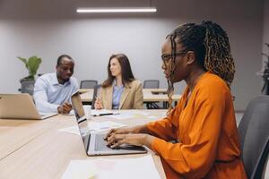 Professionals engaging in a collaborative meeting, using laptops and discussing business strategies in a contemporary office environment photo