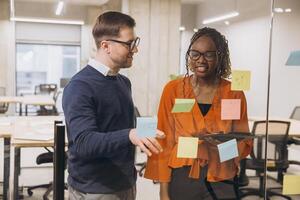 Two business professionals discussing ideas in a modern office, using sticky notes for brainstorming and project planning on a glass wall photo