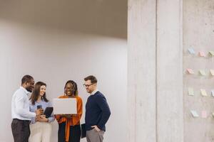 Business team collaborating, using digital devices near concrete wall, brainstorming with colorful sticky notes, modern workspace environment photo