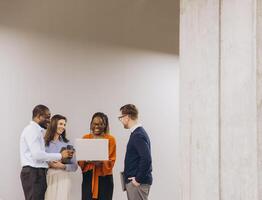 Diverse professional team collaborating, analyzing laptop project with engaged expressions in contemporary workplace environment photo
