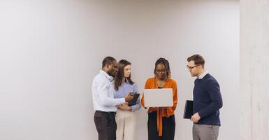 Diverse group of business professionals engaging in a collaborative discussion, focused on a laptop, in a modern office setting photo