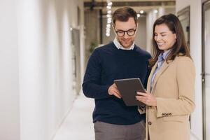 Business professionals discussing project details, leaning over tablet near office windows, displaying collaborative workplace communication photo