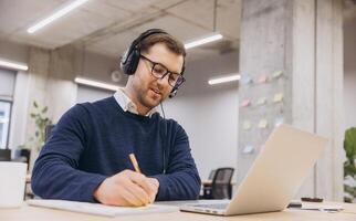 Professional employee participating in virtual conference, typing notes on laptop within contemporary, tech enabled work environment photo