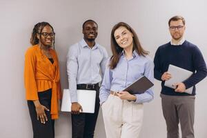 Group of diverse business professionals standing confidently with laptops and tablets, showcasing teamwork and modern workplace collaboration photo