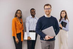 Group of diverse business professionals standing confidently with laptops and tablets, showcasing teamwork and collaboration in a modern office setting photo