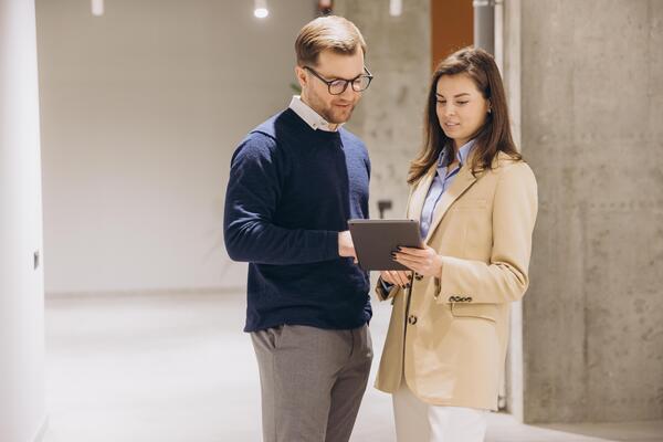 Two business partners discussing a project while using a tablet in a bright office hallway, showcasing collaboration and teamwork